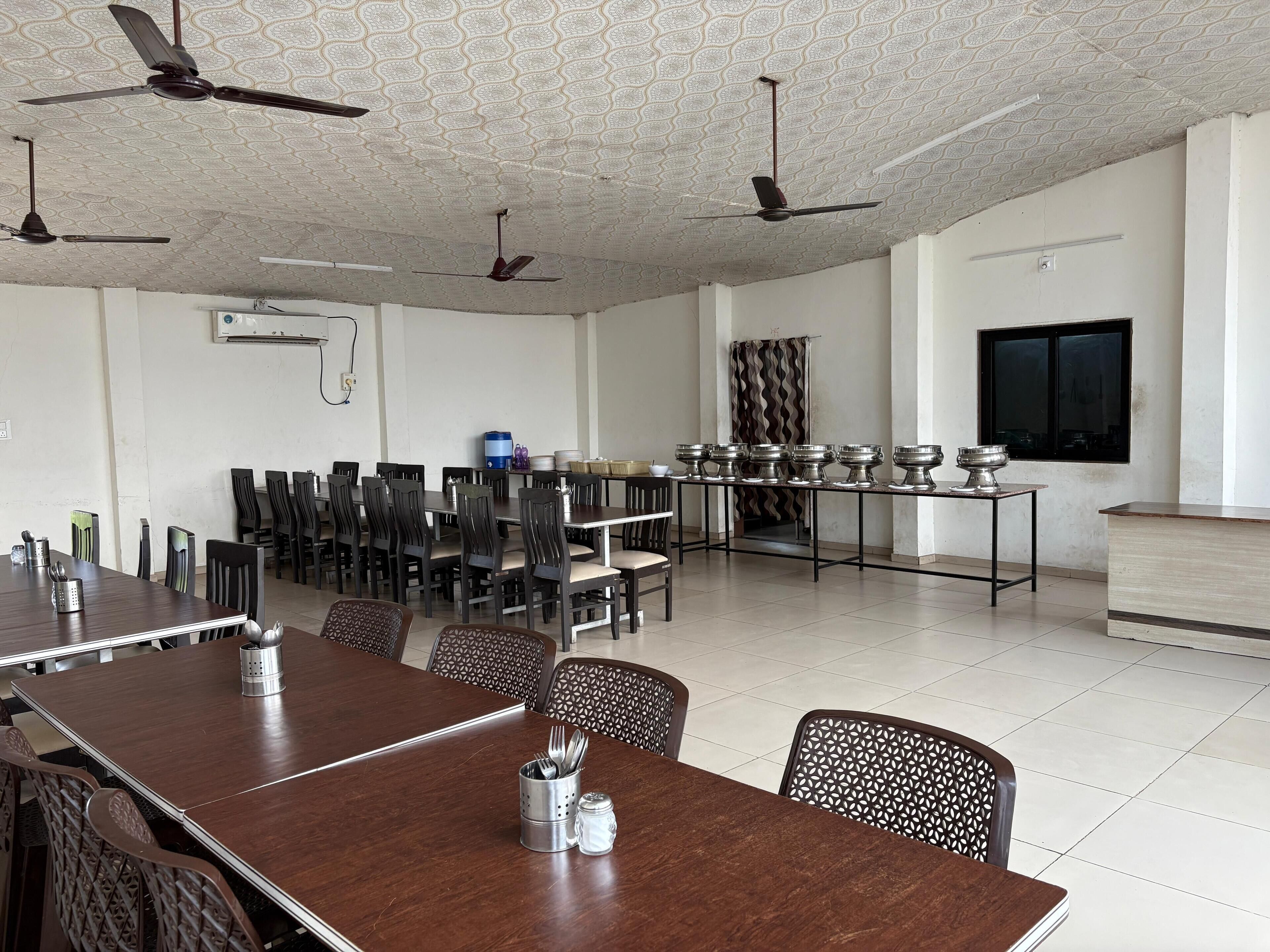 A spacious dining area with multiple tables and chairs, ceiling fans, and a large window.