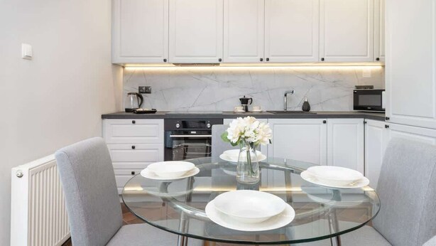 A modern kitchen with white cabinets, a glass dining table, and a vase of flowers.