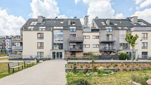 A modern apartment building with multiple balconies, a paved walkway, and a landscaped garden area.
