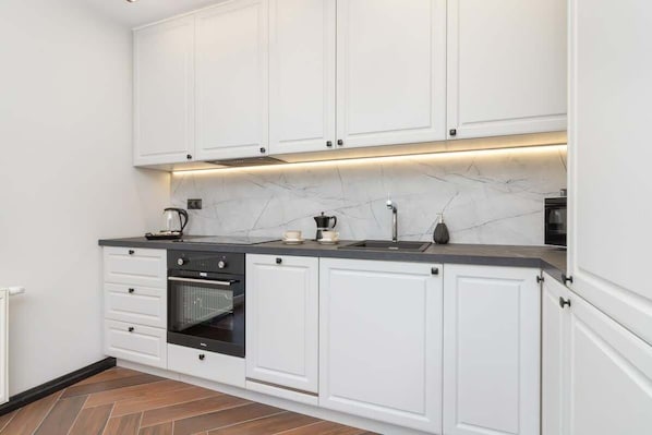A modern kitchen with white cabinets, a black countertop, and a marble backsplash.
