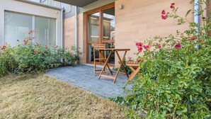 A modern outdoor patio with a wooden table and chairs, surrounded by lush greenery and flowering plants.
