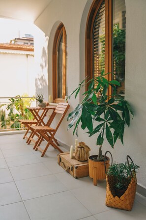 Un balcón con mesa y sillas de madera, plantas en macetas y una maleta.