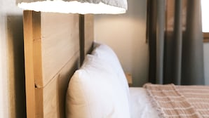 Ein Bett mit hölzernem Kopfteil, einem weißen Kopfkissen und einer strukturierten Lampe darüber.