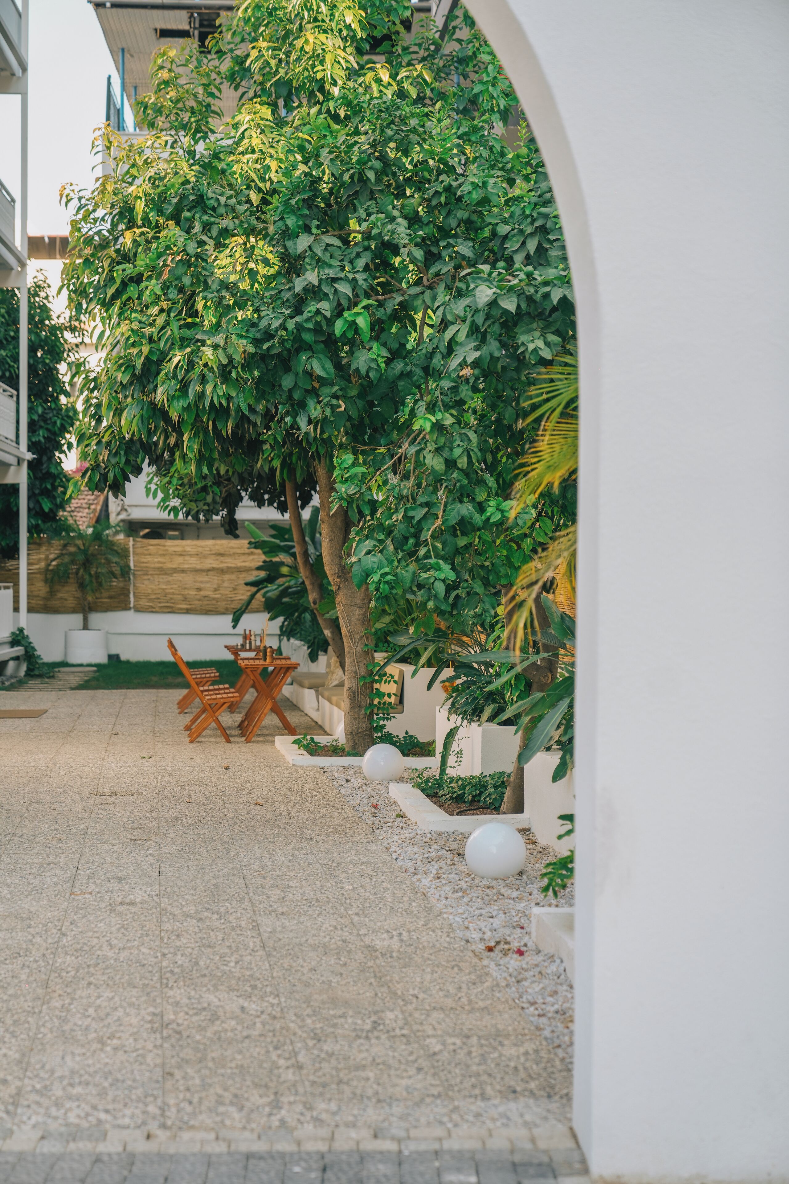 Un patio con una mesa y sillas, rodeado por un muro blanco y vegetación.