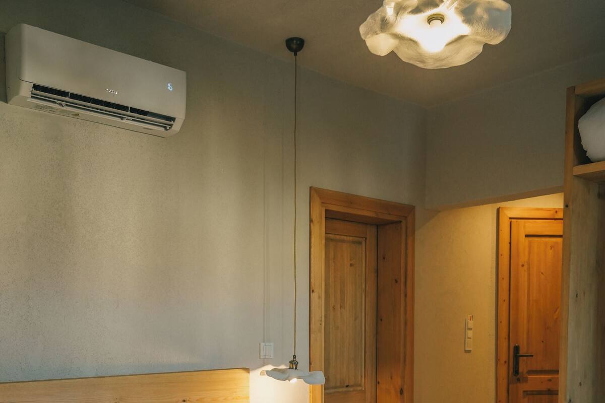Ein Hotelzimmer mit Bett, Holz-Kopfteil, Wand-Klimaanlage, Holztür und einer Pendelleuchte.