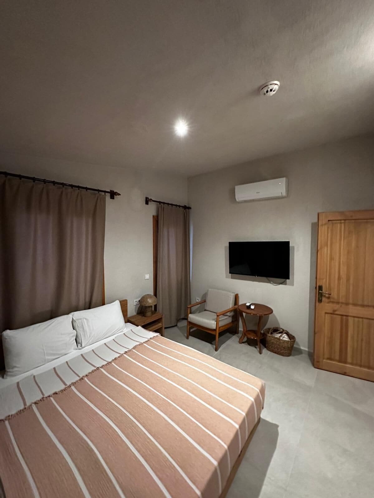 A hotel room with a bed, a chair, a small table, a television, and a wardrobe.