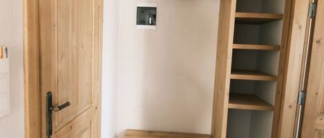 A compact room with a wooden bunk bed, a small shelf unit, and a door.