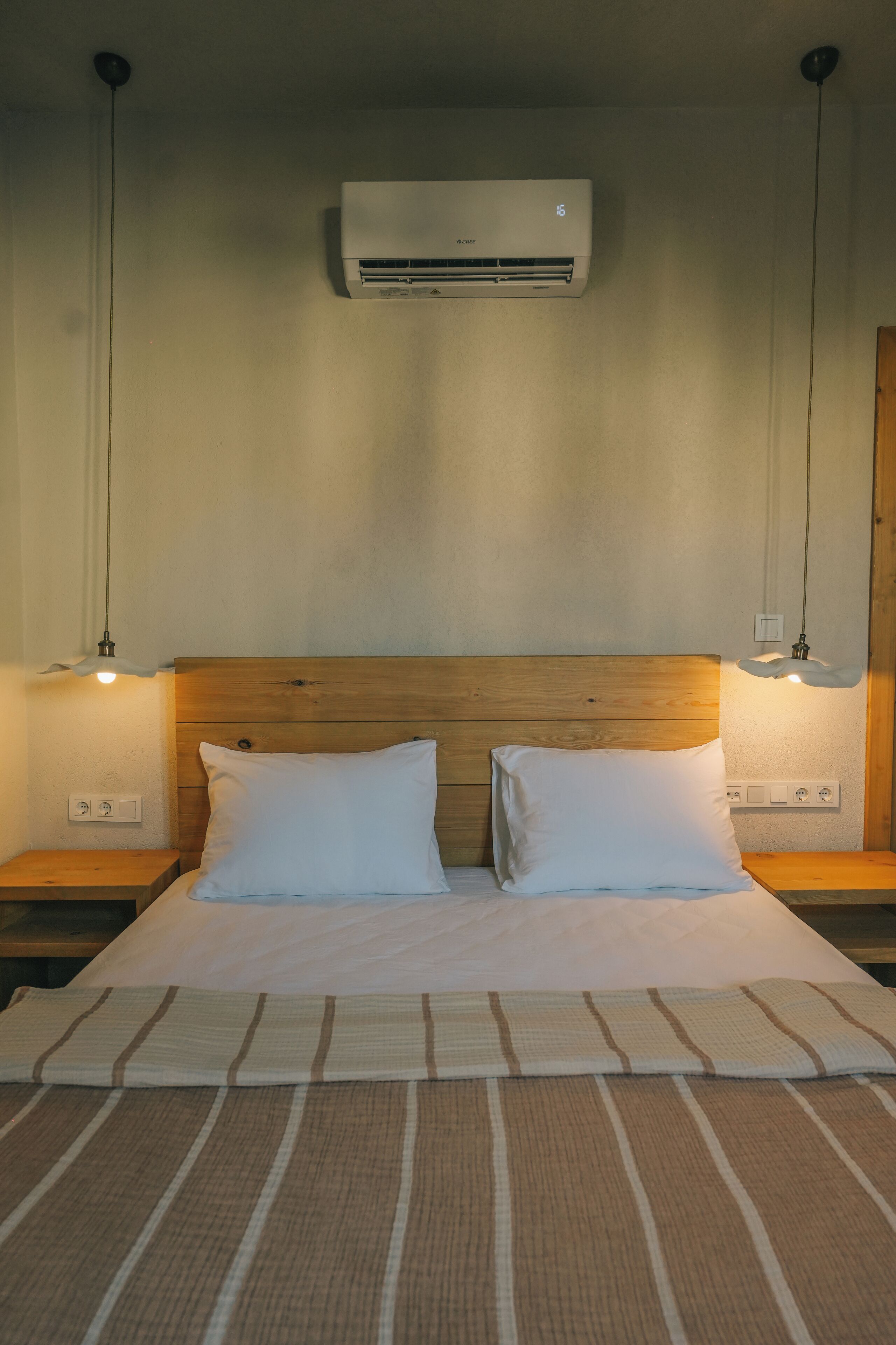 A bedroom with a wooden headboard, two white pillows, a striped bedspread, and two bedside lamps.