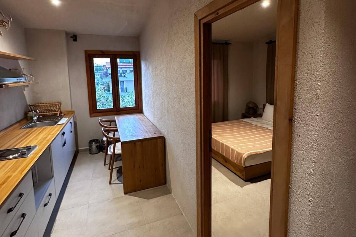 Eine kompakte Küche mit Holzarbeitsplatte und Schränken, ein kleiner Essbereich mit einer Bank sowie ein Schlafzimmer mit einem Einzelbett.