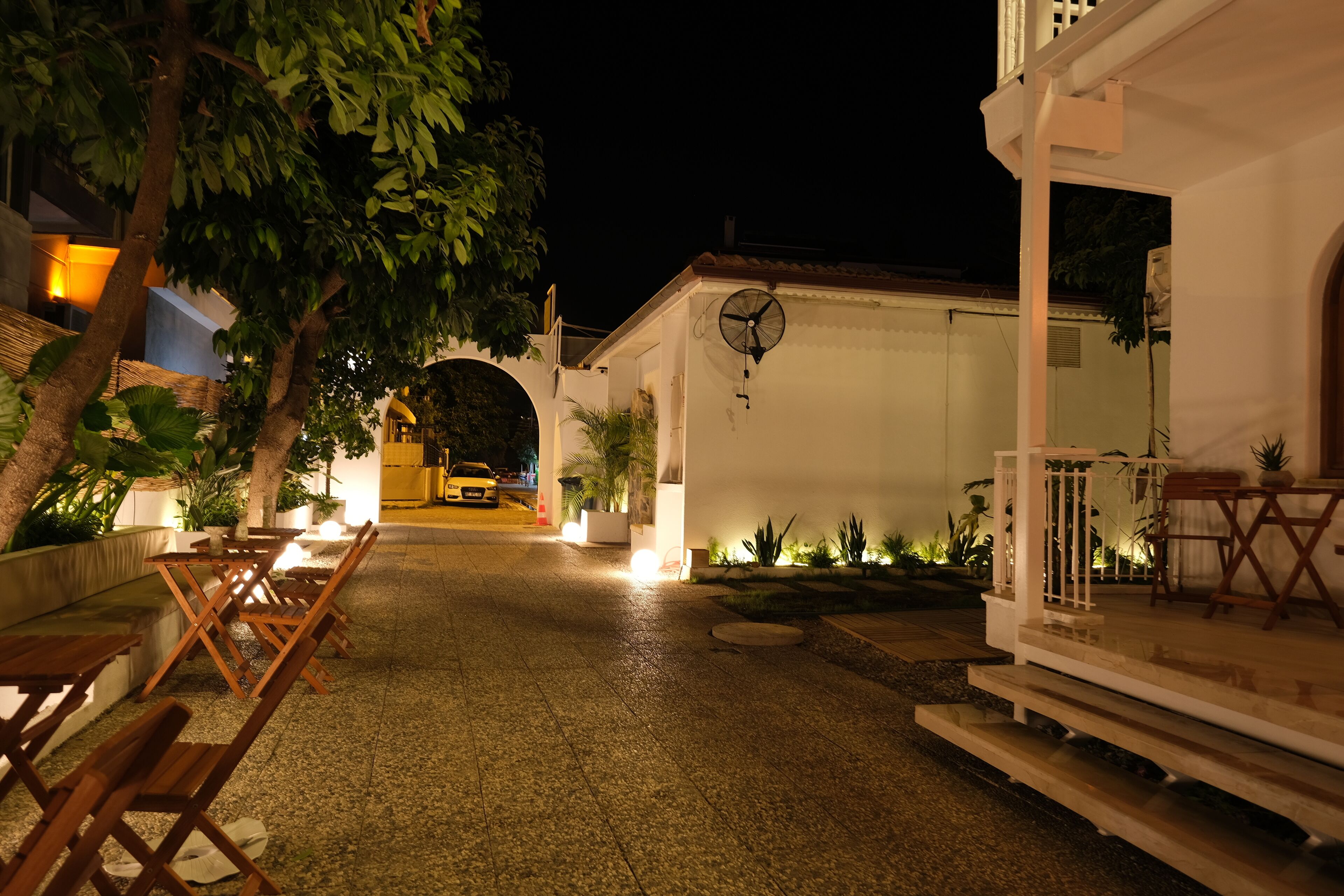 An outdoor area with wooden tables and chairs, a white building with a satellite dish, and a paved walkway.