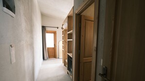Un couloir étroit avec une porte en bois sur la droite, une fenêtre avec des rideaux et une porte sur laquelle est accroché un porte-manteau.