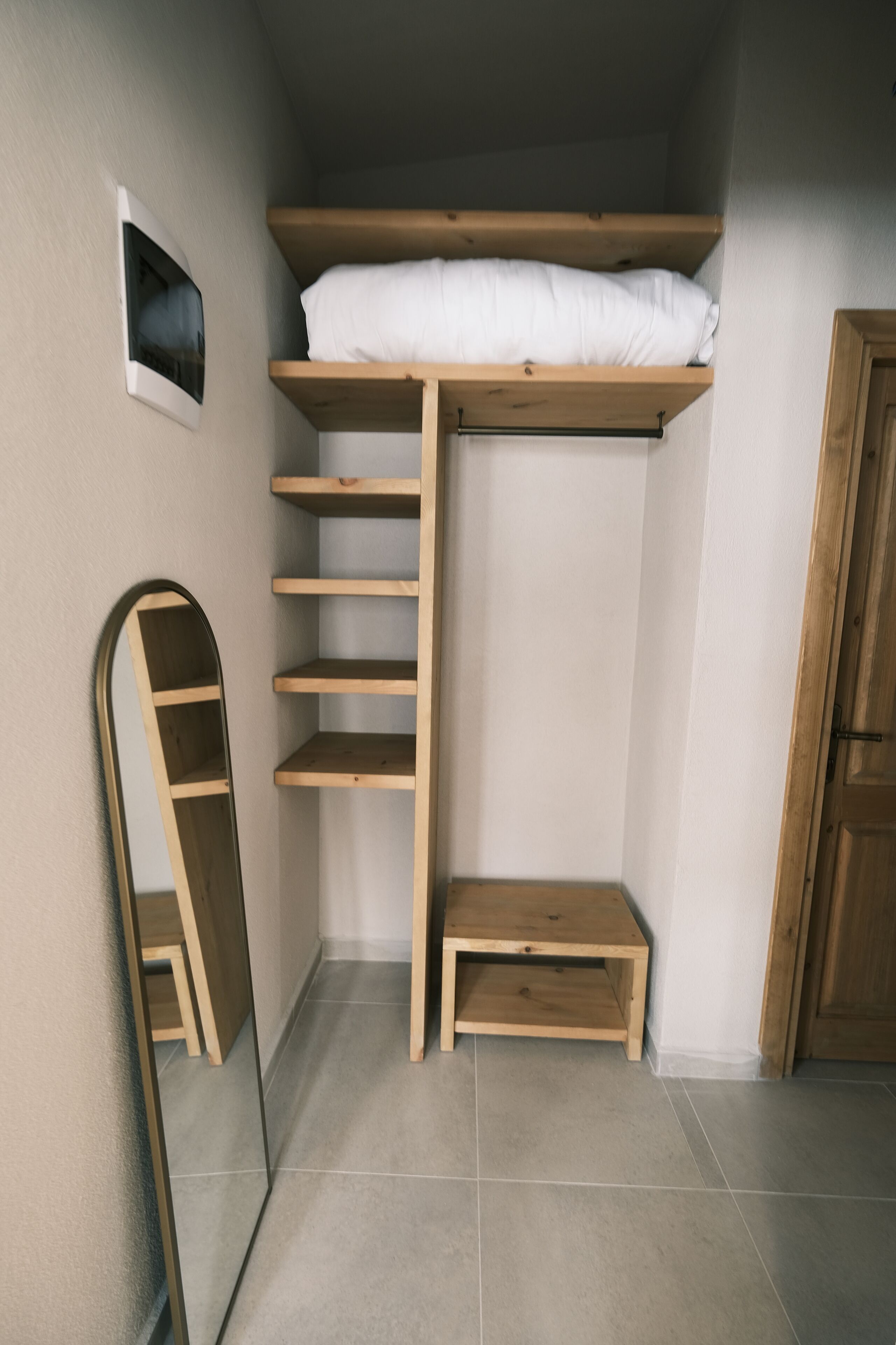 Una habitación pequeña con una cama litera, un estante de madera, una mesita de madera y un espejo.