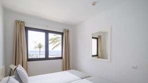 A hotel room with two beds, a window with curtains, a bedside lamp, and a small mirror on the wall.