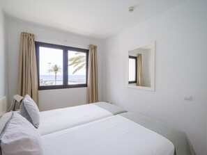 A hotel room with two beds, a window with curtains, a bedside lamp, and a small mirror on the wall.
