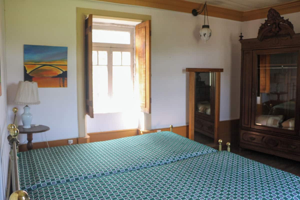 Une chambre à coucher avec un lit, une armoire en bois, un tableau et une fenêtre avec des rideaux.