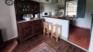 A kitchen with wooden cabinets, a microwave, and a window with curtains. - Casa Campo das Bizarras (Castro Daire)
