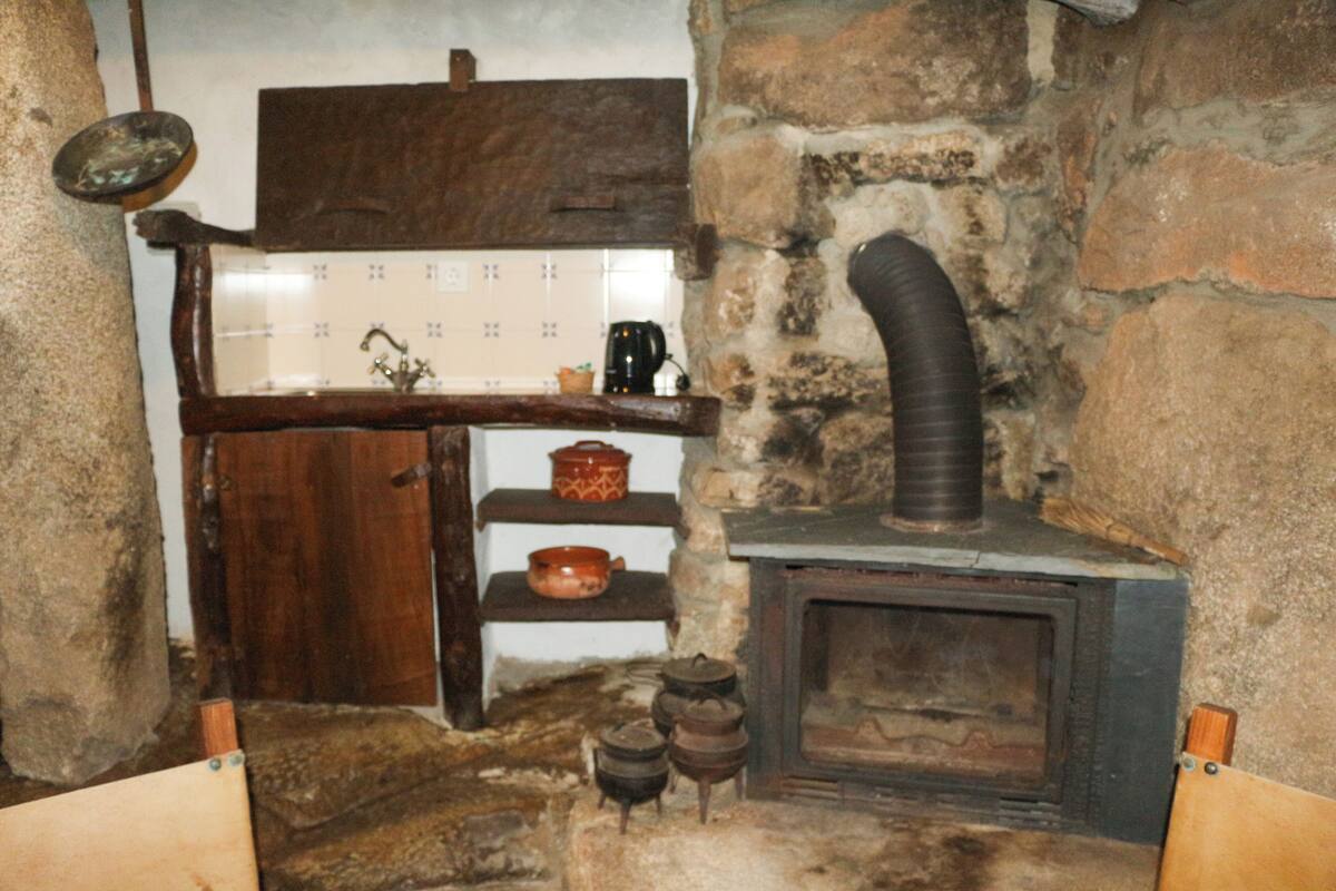 Une cuisine rustique avec un mur en pierre, des étagères en bois, un poêle et divers ustensiles de cuisine.