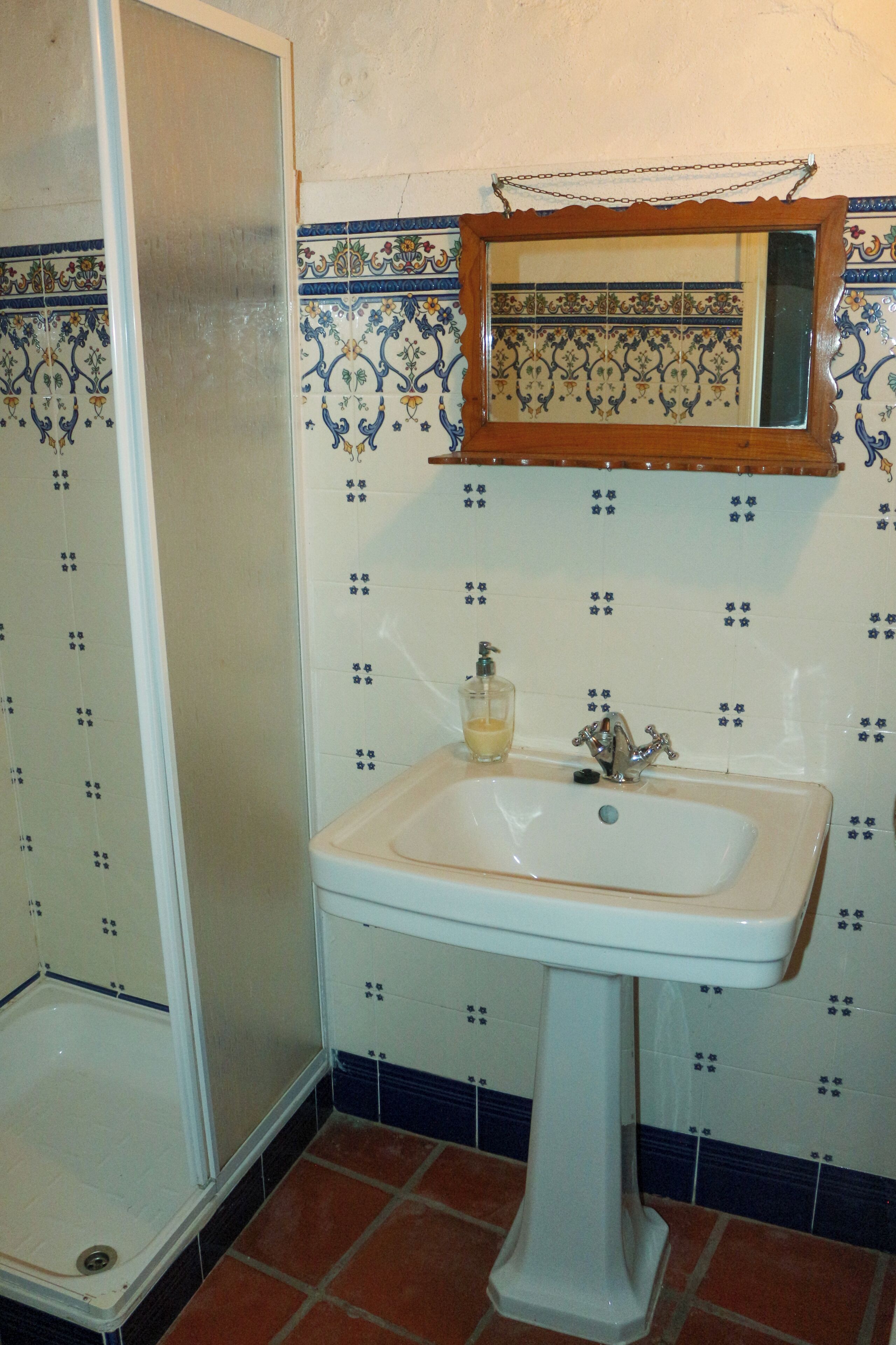 A bathroom with a white pedestal sink, a mirror above it, and a shower enclosure.