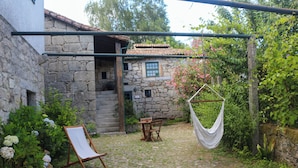 A stone building with a tiled roof, a wooden table and chair, a hammock, and a white canvas swing. - Casa Campo das Bizarras (Castro Daire)