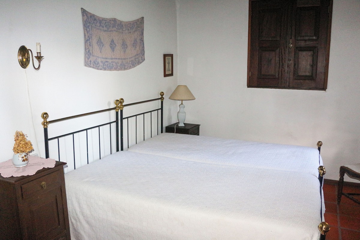 Une chambre à coucher comprenant un lit, une table de chevet, une lampe, une tapisserie murale et une porte.