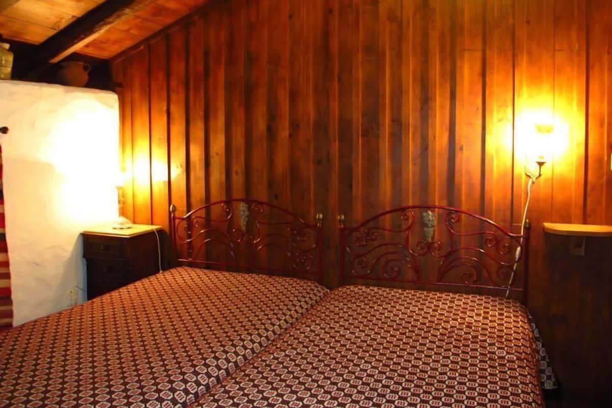 Une pièce aux murs en bois, avec un lit en métal et deux lampes de chevet.