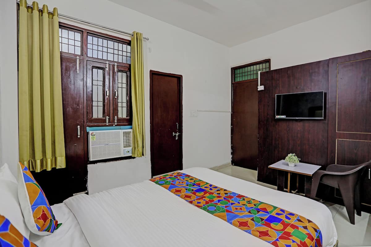 A hotel room with a bed, a TV mounted on the wall, a small table with a plant, and a chair.