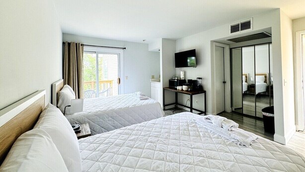 A hotel room with two beds, a TV, a desk with a coffee maker, and a sliding door leading to a bathroom. - Bay Tree cozy studio in Little River (Little River)