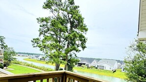 A wooden deck with two chairs and a table, overlooking a residential area with houses and a large tree. - Bay Tree cozy studio in Little River (Little River)