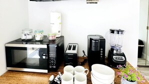 A kitchen with a flat-screen TV, microwave, toaster, coffee maker, blender, and various kitchen items on a wooden countertop. - Bay Tree cozy studio in Little River (Little River)