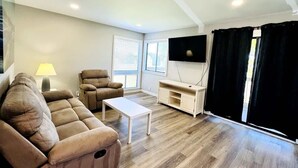 A living room with a sectional sofa, a coffee table, a TV, and a sliding door with curtains. - Bay tree lovely one bedroom condo (Little River)