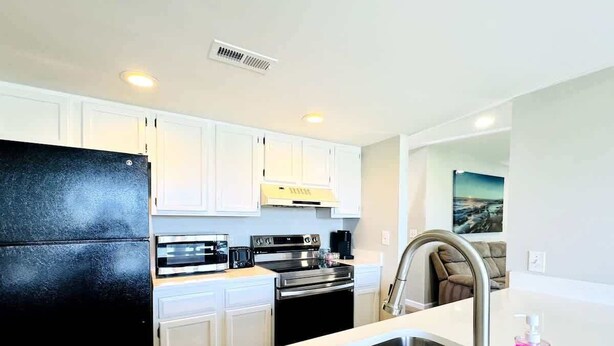 A modern kitchen with white cabinets, stainless steel appliances, and a black refrigerator. - Bay tree lovely one bedroom condo (Little River)