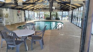 A pool area with a round table and chairs, surrounded by glass walls and a covered roof structure. - Bay tree lovely one bedroom condo (Little River)