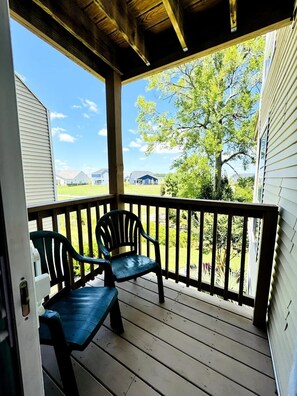 Une véranda abritée, avec deux chaises et une table, donnant sur un quartier résidentiel avec des maisons et des arbres.