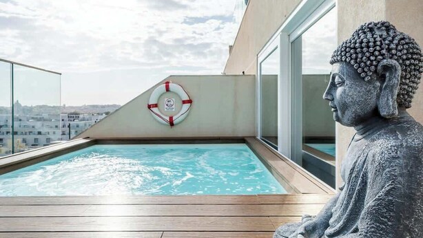 A statue of Buddha overlooking a swimming pool with a lifebuoy and a view of the cityscape.