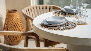 A round dining table with a white tablecloth, wooden chairs, and a woven placemat.