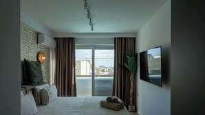 A hotel room with a bed, a television, a large window, and a view of the city.