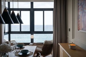 A dining area with a table set for two, a view of the sea through large windows, and a candle on the table.