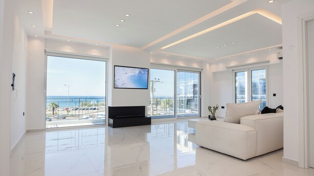 Ein geräumiges Wohnzimmer mit großem Fernseher, weißen Möbeln und Blick auf den Ozean.