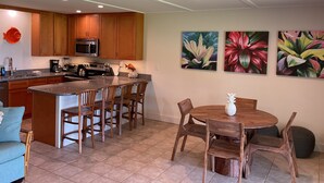 A modern kitchen with wooden cabinets, a central island, and a dining area with a round table and chairs. - Ma'alaea Surf Unit F3-1 BR Ground Floor Beachfront Condo, Wi-Fi, AC, Pool, TV (Kihei)