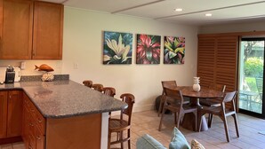 A kitchen with wooden cabinets, a granite countertop, and a dining area with wooden chairs and a table. - Ma'alaea Surf Unit F3-1 BR Ground Floor Beachfront Condo, Wi-Fi, AC, Pool, TV (Kihei)