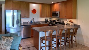A modern kitchen with wooden cabinets, stainless steel appliances, and a granite countertop. - Ma'alaea Surf Unit F3-1 BR Ground Floor Beachfront Condo, Wi-Fi, AC, Pool, TV (Kihei)