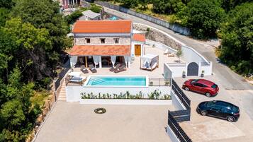 A two-story house with a swimming pool, a covered patio, and a red car parked in the driveway.