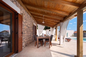A covered outdoor dining area with a stone wall, wooden ceiling, and a view of a swimming pool. - Casa di Nika Stone Villa With Pool & Jacuzzi (Vinodol)