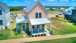 A two-story house with a covered porch and a small deck, surrounded by a well-maintained lawn and a clear sky. - Just Peachy (Carlton landing)