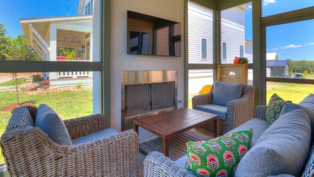 A spacious outdoor living area with wicker furniture, a wooden table, and a large window offering a view of a house and greenery. - Just Peachy (Carlton landing)