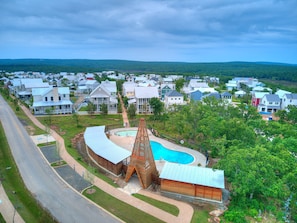 A residential area with a swimming pool, a unique wooden structure, and houses with various roof styles.