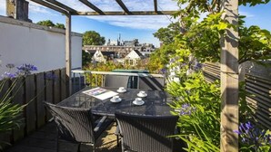 Un patio al aire libre cubierto con una mesa y sillas, rodeado de plantas y vistas a la ciudad.