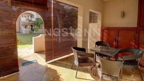 Un'area patio con mobili in vimini e un tavolo in vetro, una porta scorrevole e vista su un edificio sullo sfondo.