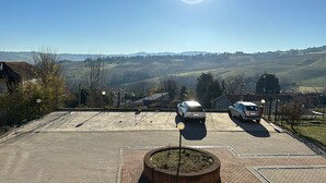 A parking area with two cars, a brick pathway, and a view of distant hills and buildings. - House at the Knoll (Montescano)