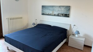 A bedroom with a bed, a nightstand, a lamp, a radiator, and a cityscape painting on the wall. - House at the Knoll (Montescano)
